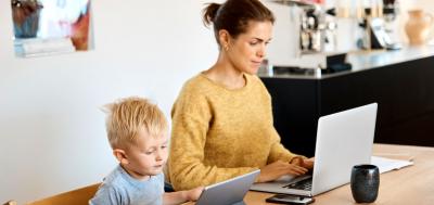 Woman working on laptop next to child using tablet at kitchen table