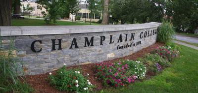 Stone sign that says Champlain College in front of campus building