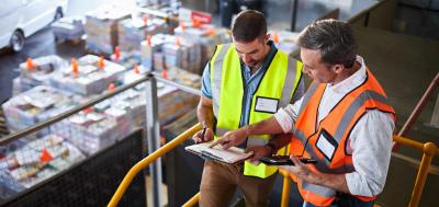 Two supply chain managers in warehouse looking at clipboard