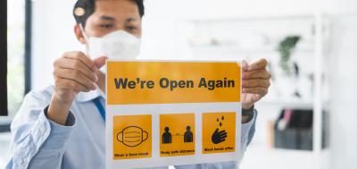 Asian businessman wear face mask attach reopen sign at office after lockdown due to coronavirus covid-19, business new normal and social distancing concept.