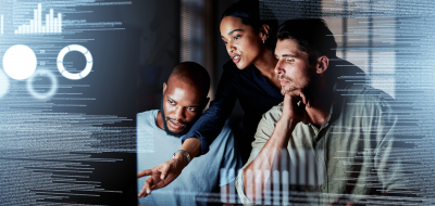 two men and a woman in a dark room looking at a computer monitor