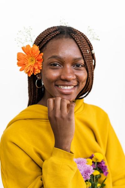 An African American woman poses for headshot with a yellow hoodie and orange flower in her ear.