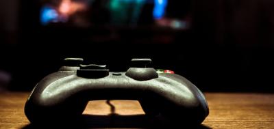 Video game controller on a table in front of blurred TV