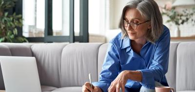 Mature woman studying on laptop and writing in notebook