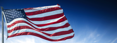 American flag blowing in wind, blue sky in background