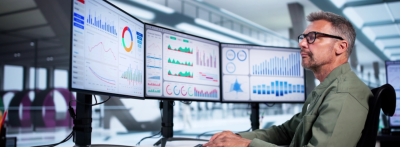 business analyst working at computer with various charts and graphs on screen