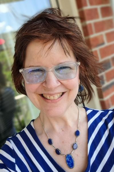 Woman with short, red hair and glasses smiling at camera.