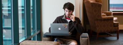 Teen male student studying at desk with open latop