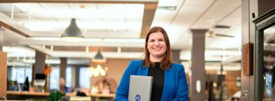 Woman standing in library holding laptop smiling portrait