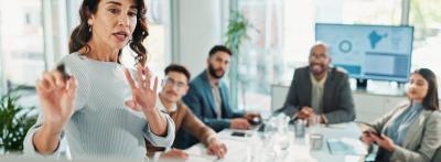 A woman at the head of a conference table while four colleagues listen attentively