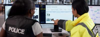 Police detectives reviewing digital case management and evidence software on office monitors