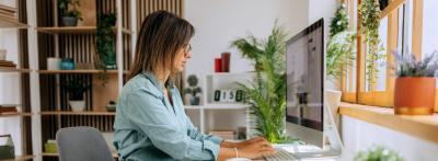 Woman working at a desktop computer at a home office desk, reviewing a digital marketing campaign