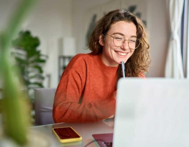 Woman smiling in front of laptop with pen in hand