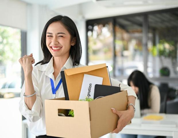 Happy newly hired female digital media professional with box of office supplies