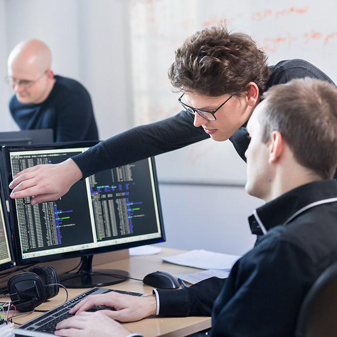 One man pointing at something on a computer screen with another man looking on