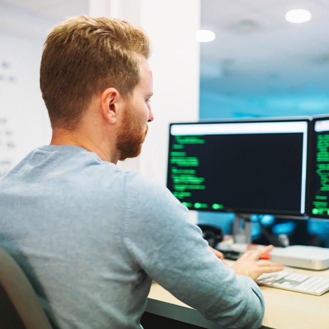 Man looking at dual computers filled with green text