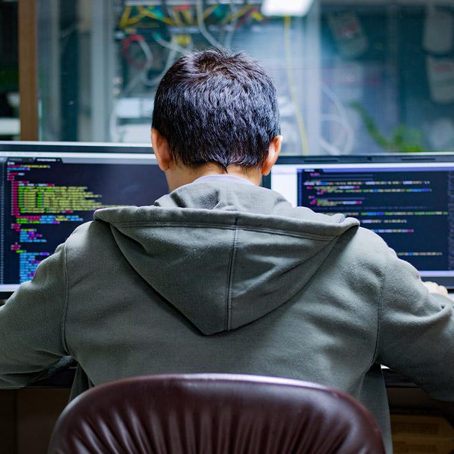 PHP programming student sitting at desk with two computer screens with code on them