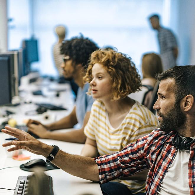 Online students discussing code on a computer in a computer lab