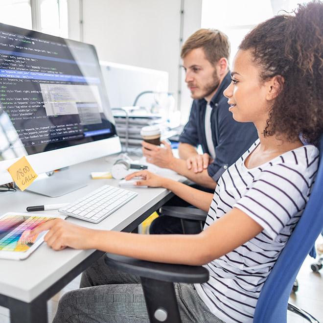 Software development online bachelor's degree graduate collaborating with colleague in front of computer