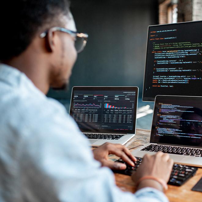 Web Design & Development professional at the office in front of multiple computer screens writing code