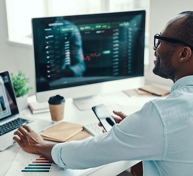 African american man at laptop and monitor with financial data on screens