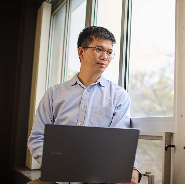 Asian man with laptop gazing out window